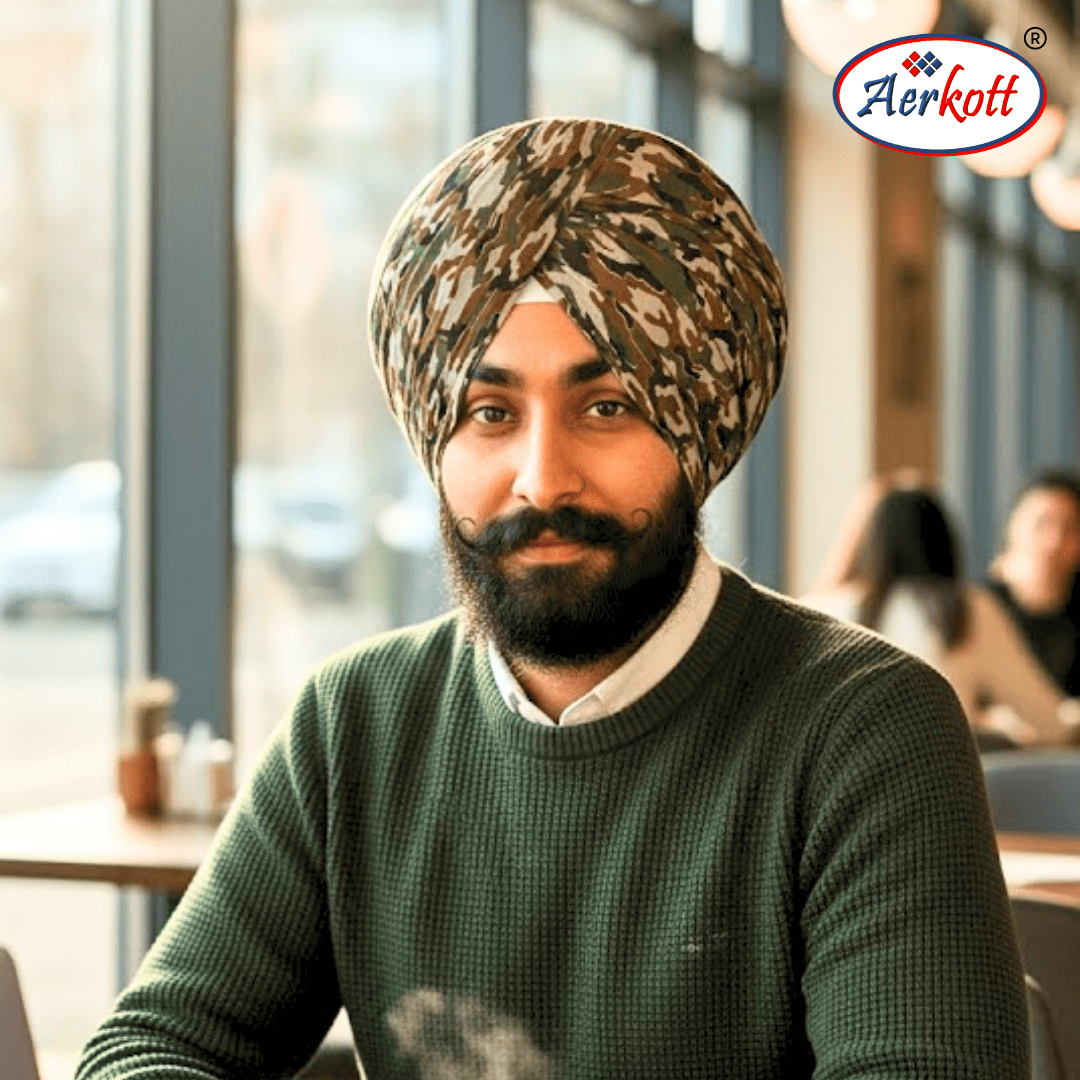 Man wearing a camouflage turban sitting in a cafe with Aerkott logo in the corner.