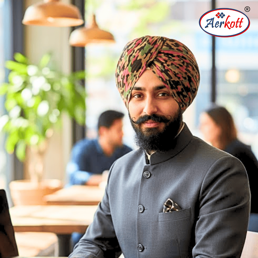 Man wearing a colorful turban and gray traditional outfit in a casual setting with 'Aerkott' branding.
